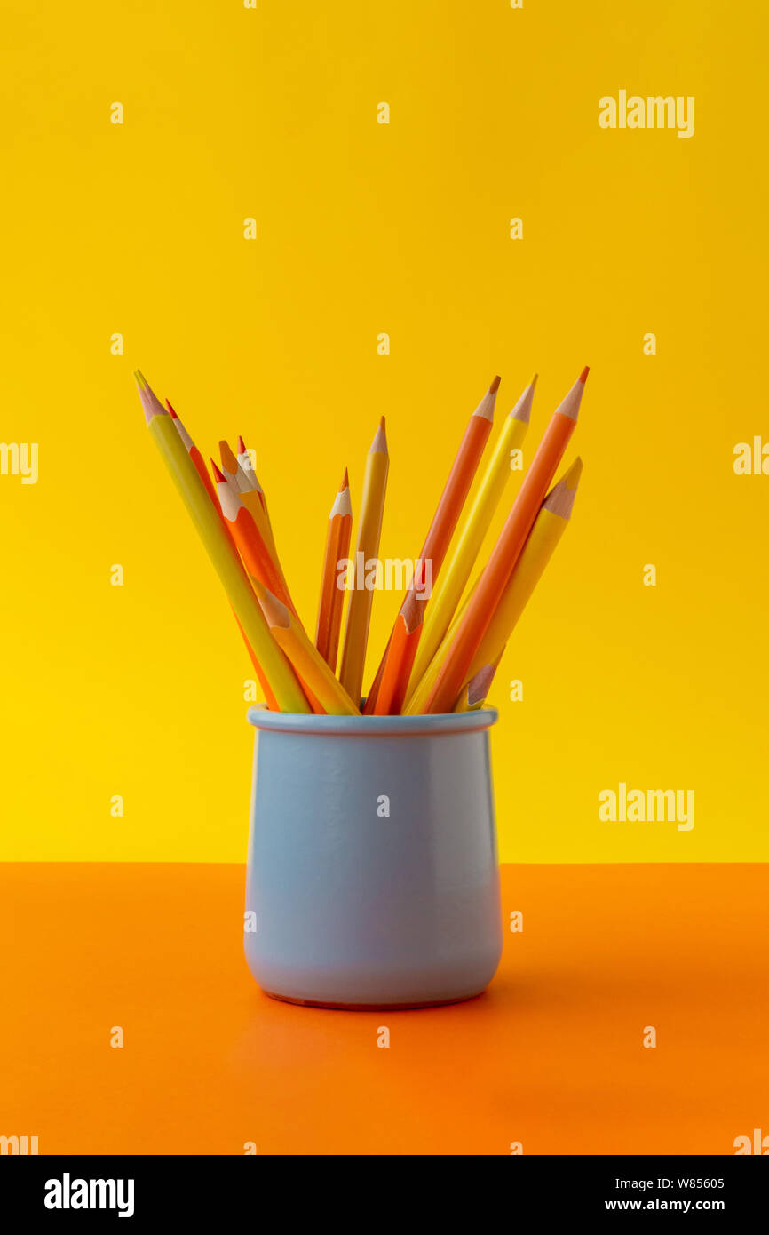 Orange and yellow pencils on bright trend background in blue ceramic holder. Stock Photo