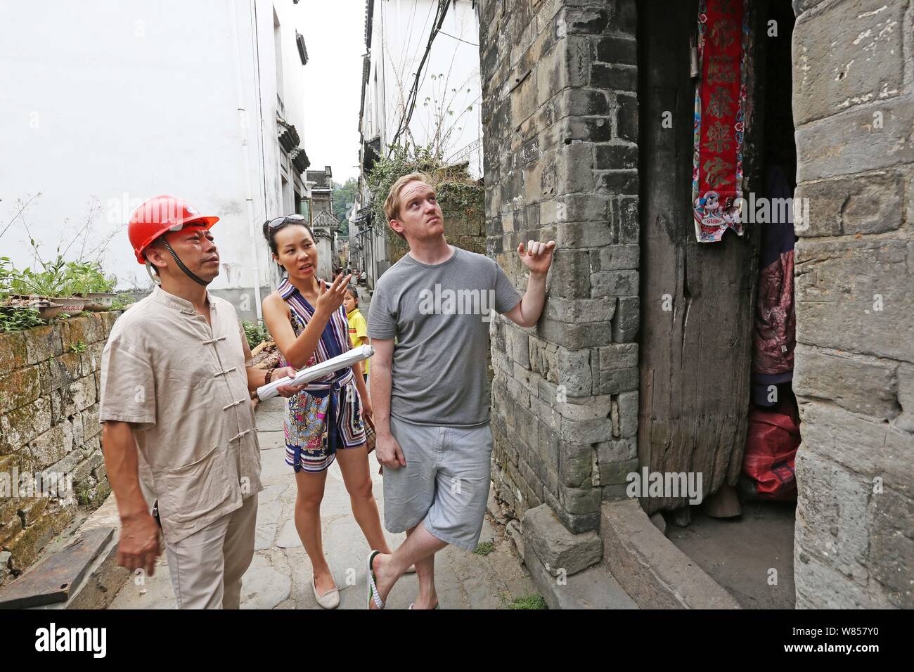 British man Edward Gawne, right, his Chinese fiancee Liao Minxin, center, and Chinese sculpting master Yu Youhong examine a damaged house from the Qin Stock Photo