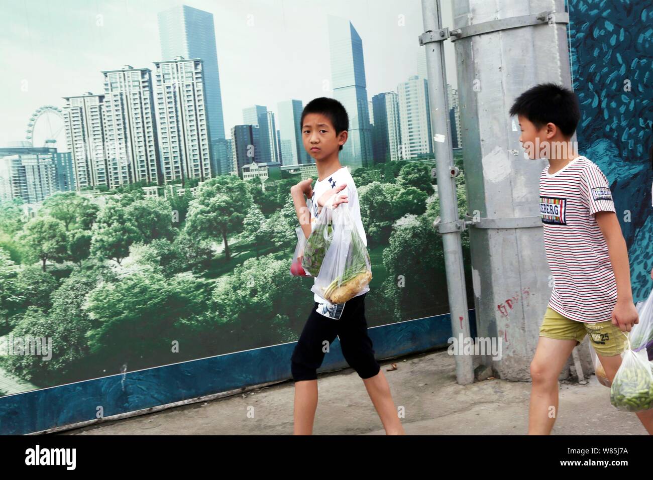 --FILE--Young Chinese boys walk past a billboard at the construction site of a residential property project in Shanghai, China, 3 August 2016.   Stron Stock Photo