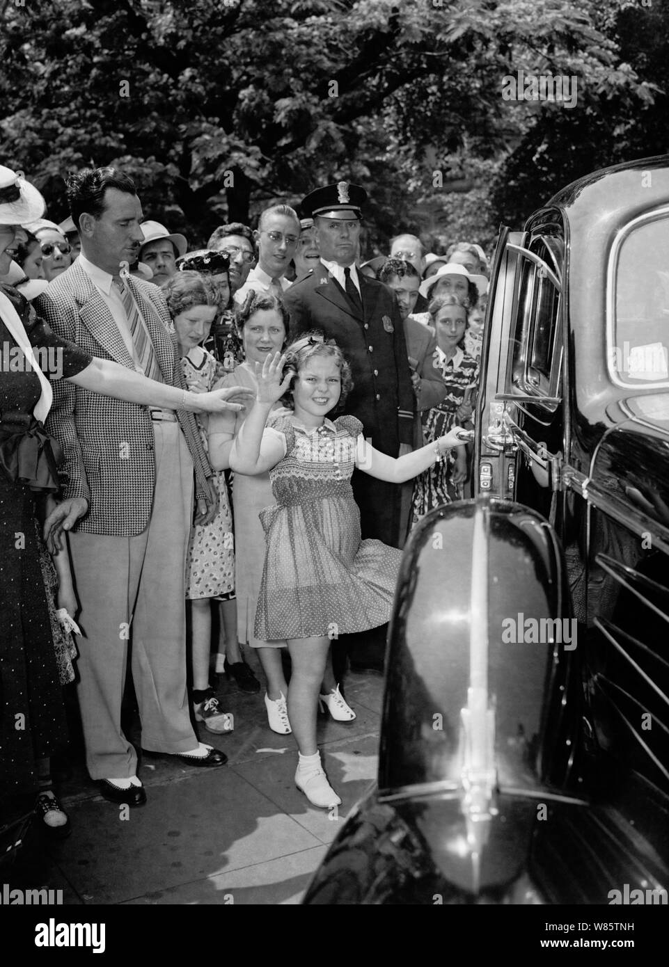 Vintage photo of American child film star Shirley Temple (1928 – 2014). The image was captured on June 24 1938 as the young actress waved to onlookers after she left the White House following a meeting with US President Franklin D Roosevelt. During their conversation she told the President how she had lost a tooth the night before when it fell out as she ate a sandwich. Stock Photo