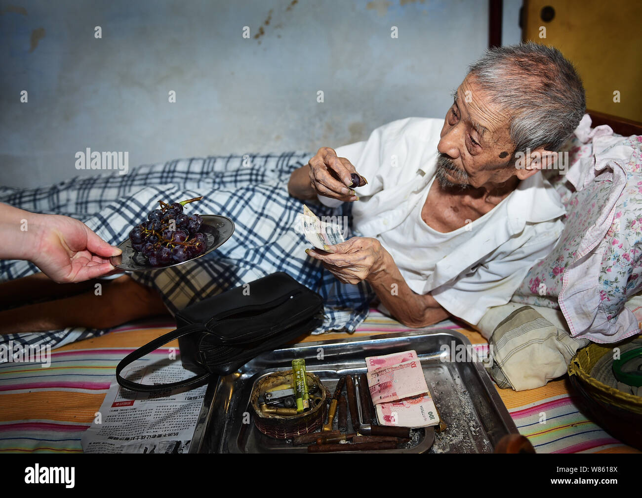 103-year-old Lin Yongqing who was a bank cashier eats grape as he counts banknotes on the bed at home in Chengdu city, southwest China's Sichuan provi Stock Photo