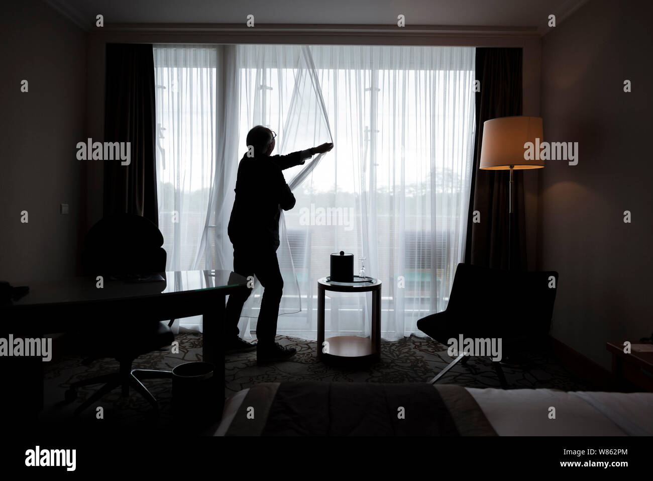 Man, alone in his living room, closing his curtains Stock Photo