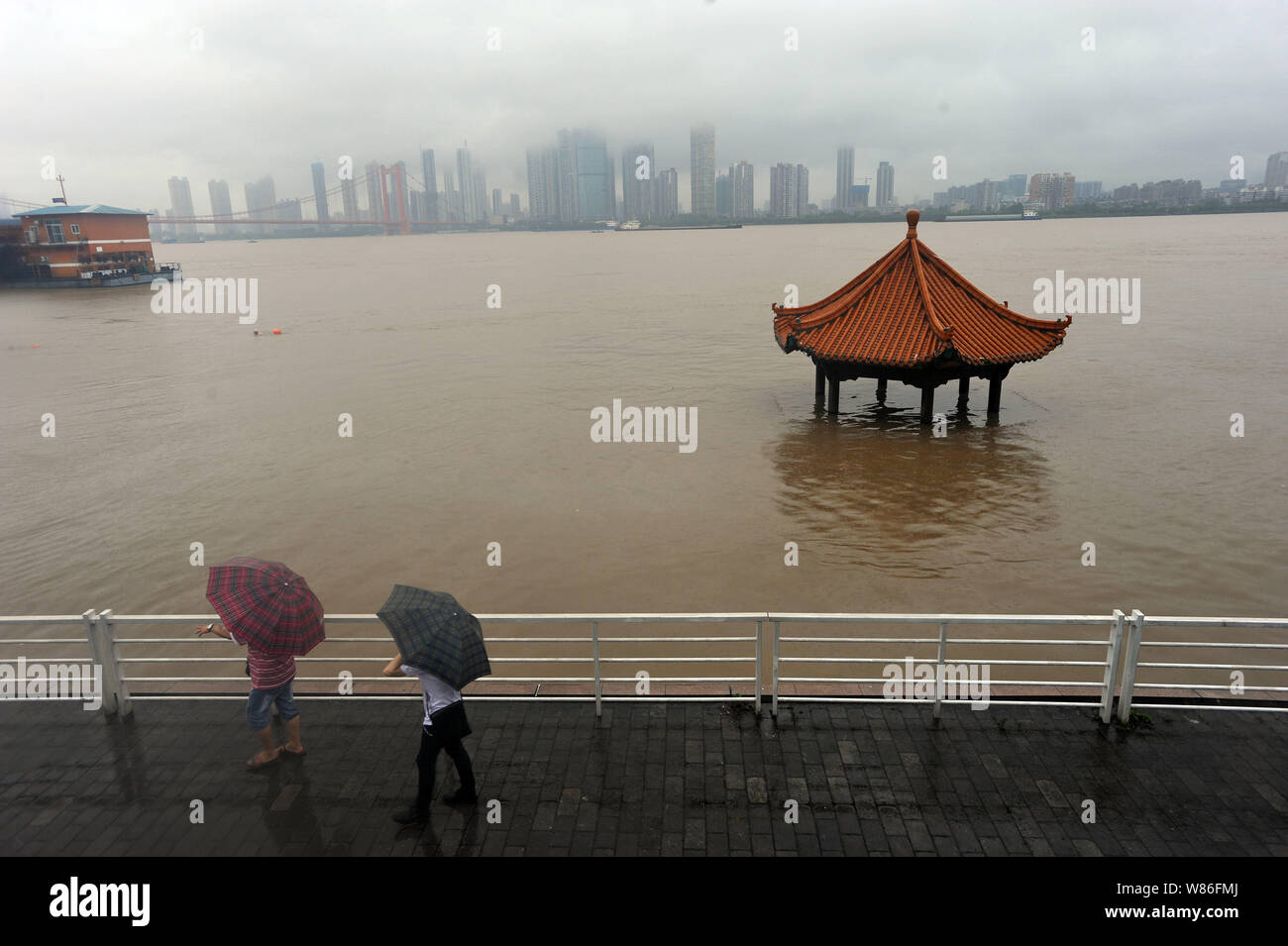 Local Chinese residents walk past a riverside pavilion submerged by the flooded Yangtze River caused by heavy rain in Wuhan city, central China's Hube Stock Photo
