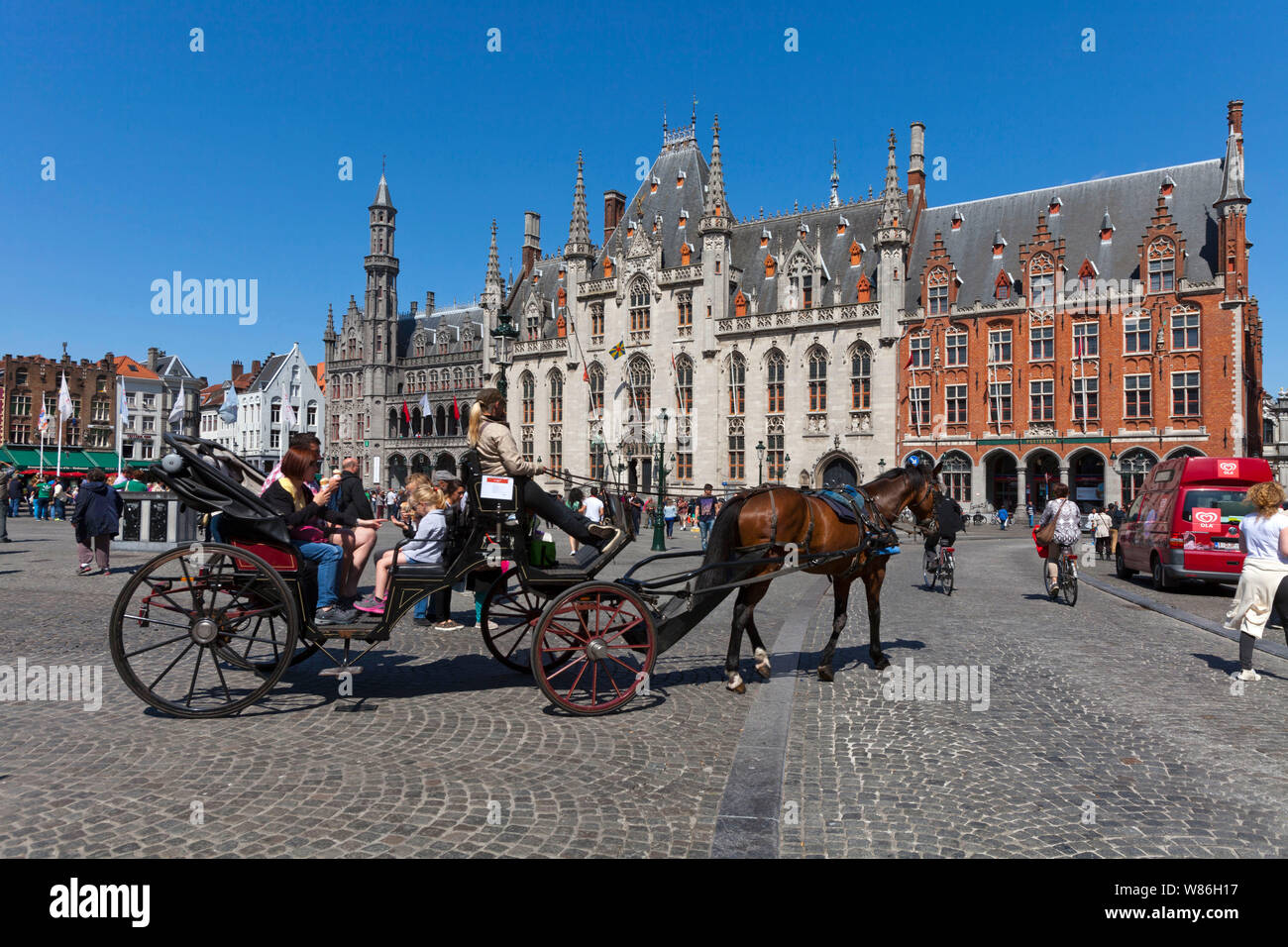 Belgium, Bruges: horse-drawn carriage in the Old City and elaborate facade of the Provincial Palace in neo-Gothic style in the main square Markt ('Mar Stock Photo