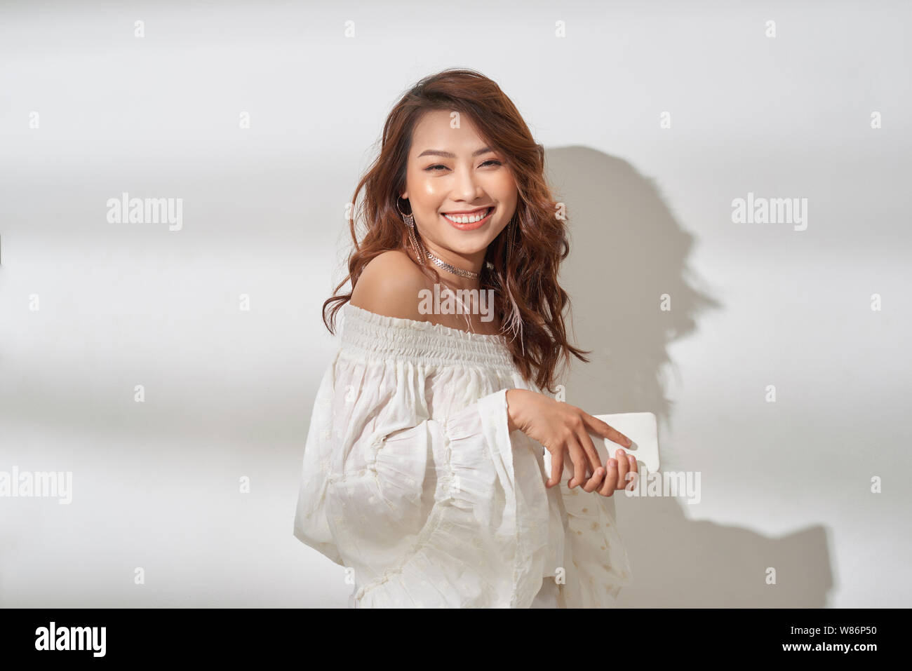 pretty asian woman in casual wear holding smartphone in one hand, dancing Stock Photo