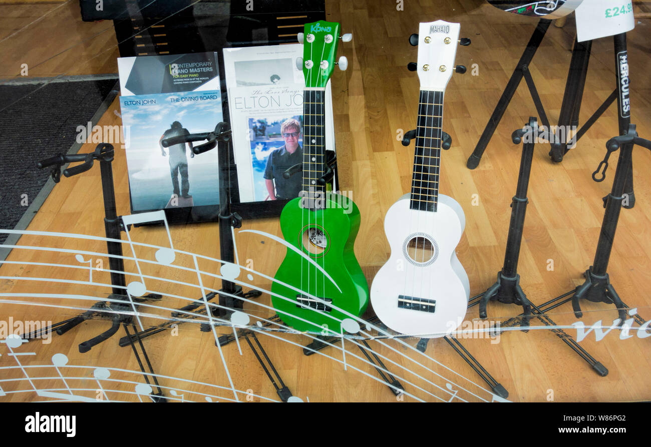 One Green and one white Ukulele in shop window with musical notes on window, Brighton East Sussex Stock Photo