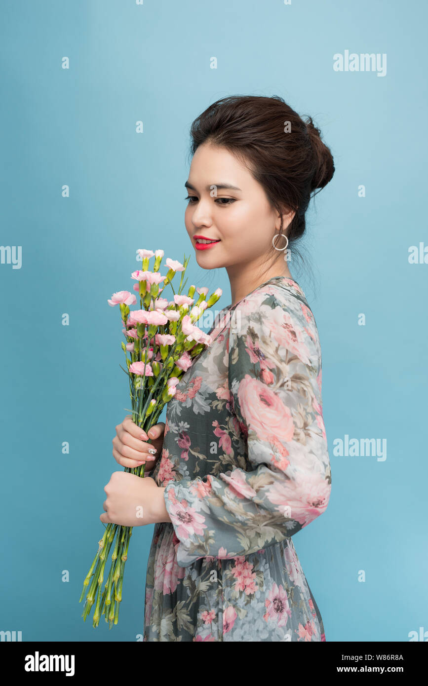 Attractive Asia woman in romantic dress holding bouquet of flowers over blue background Stock Photo