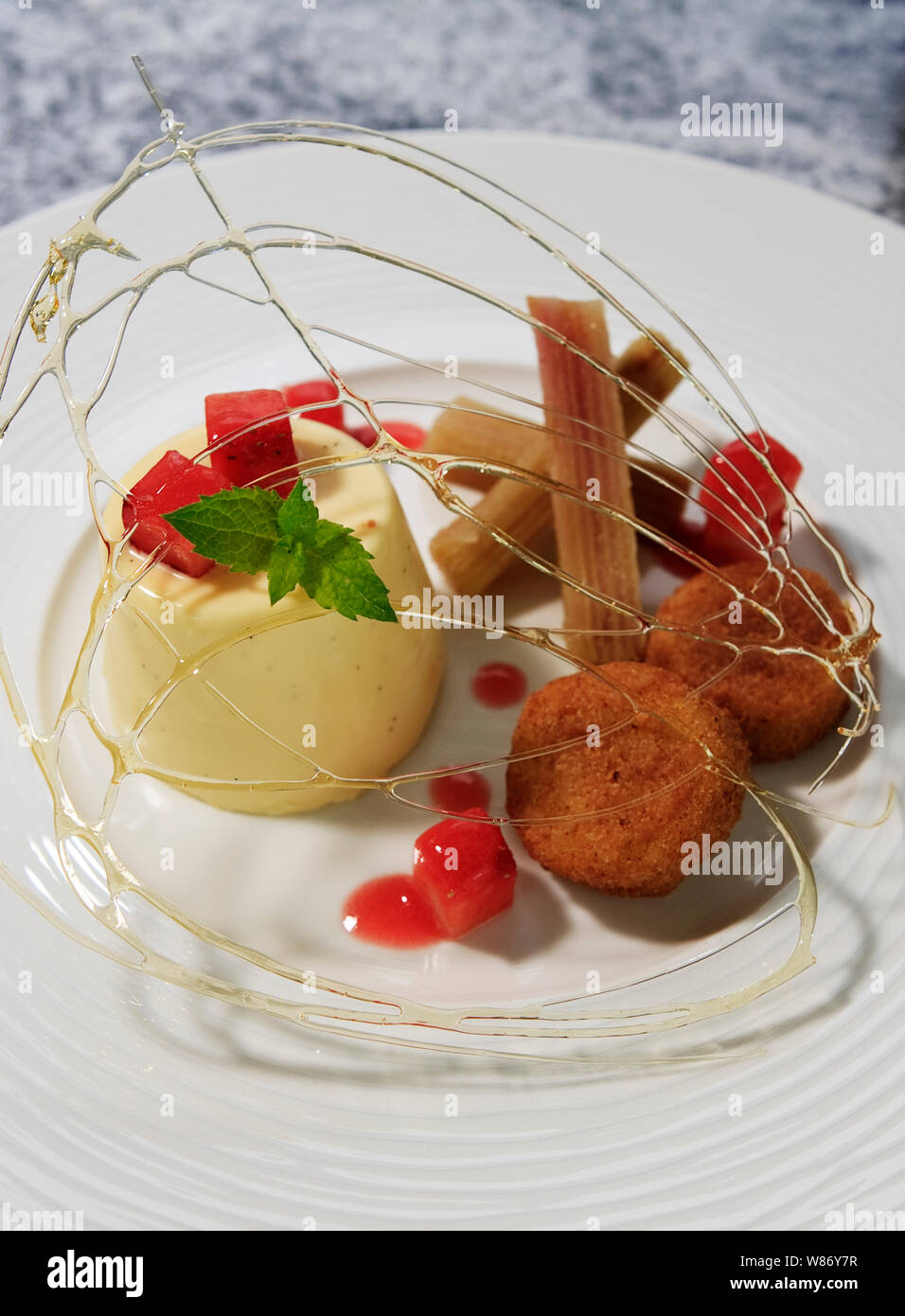 Panacotto with strawberry jellies and custard bon bons, candied sugar, churros and basil Stock Photo