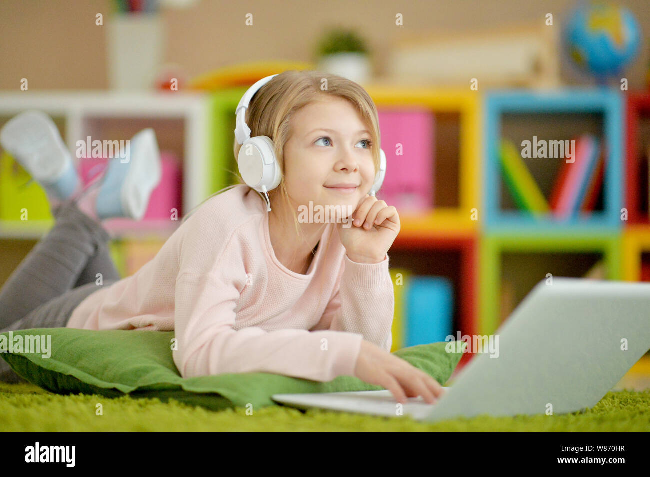 Portrait of cute girl using laptop while lying on floor with green ...