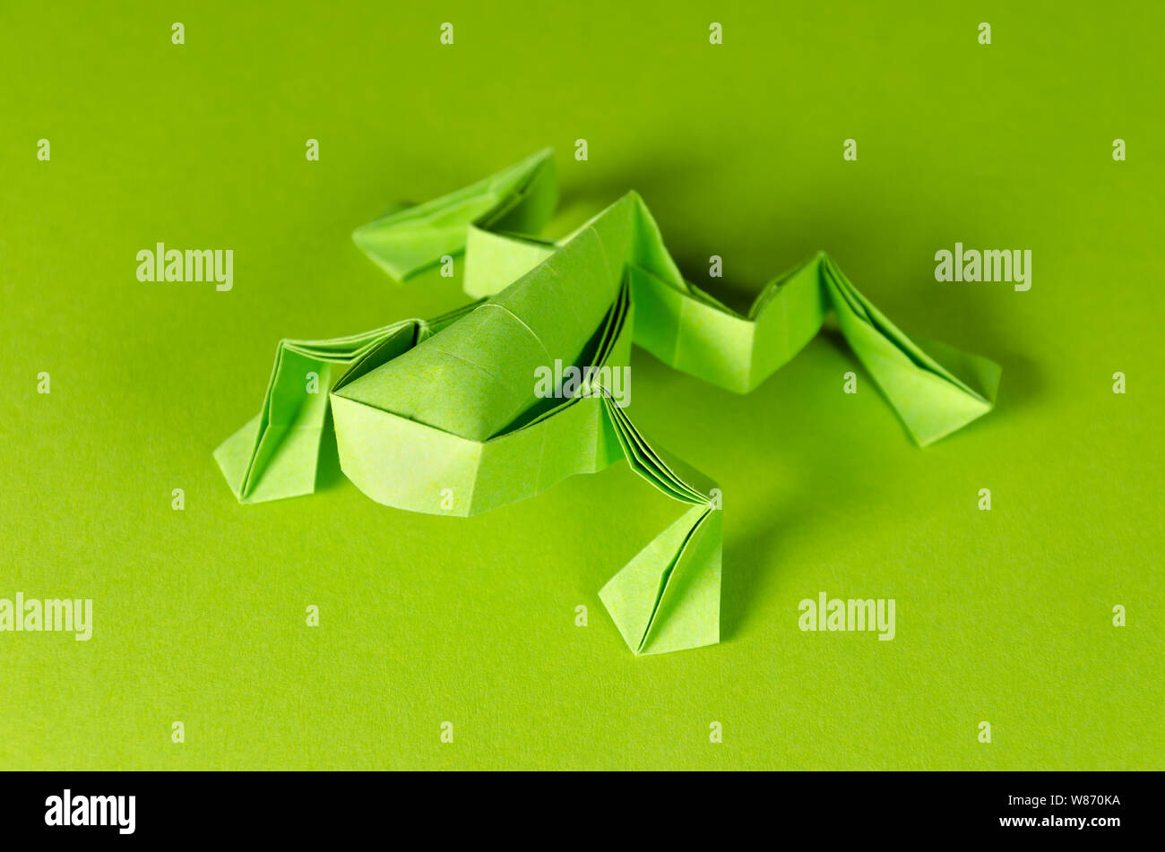 Green origami frog on green background. Japanese art of paper folding