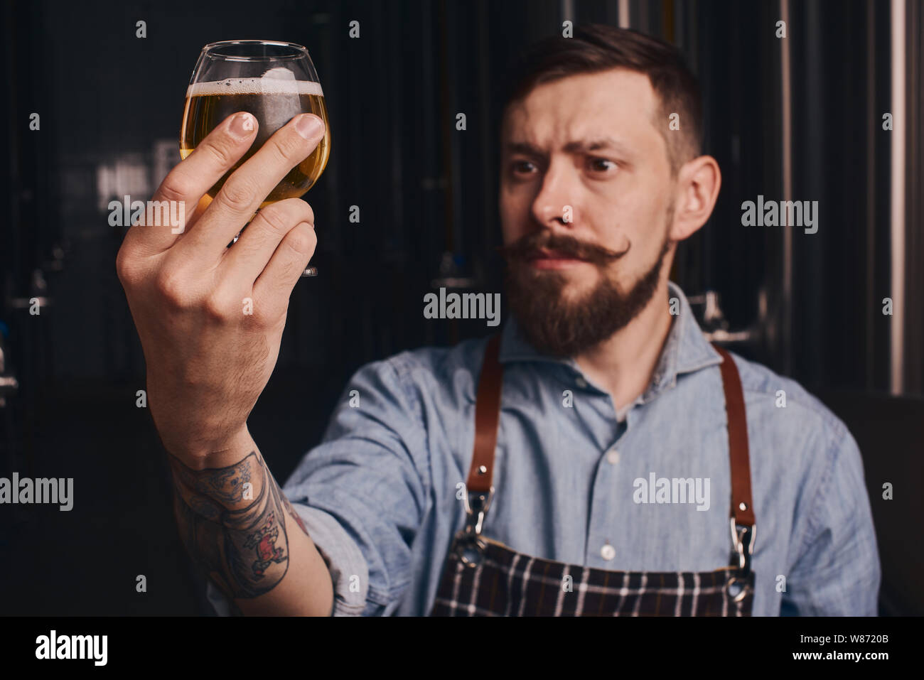 Bartender in the apron checks beer quality holding it in front of ...