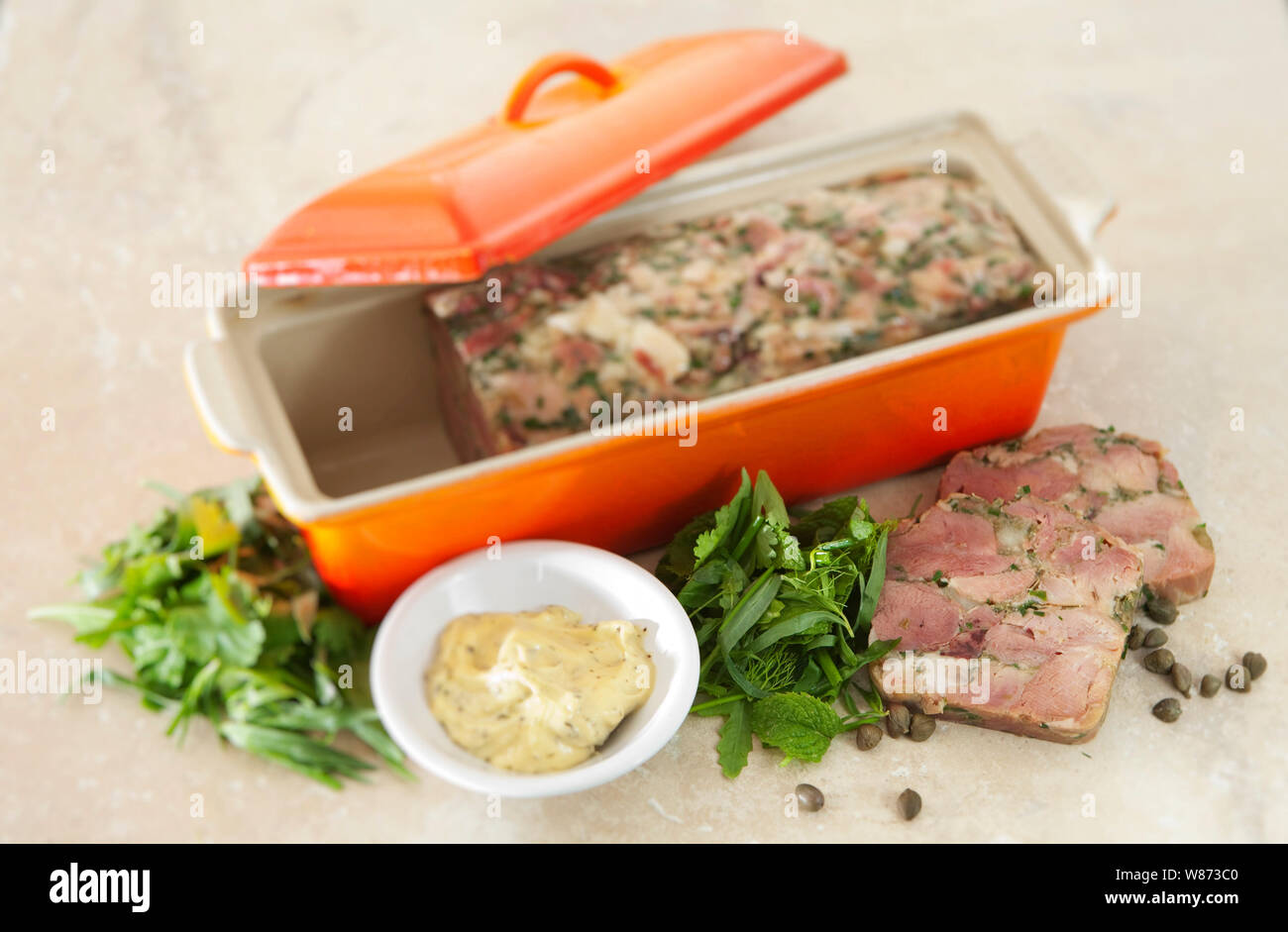 home made ham hock terrine in an orange terrine dish served with mayonnaise and herbs. Stock Photo
