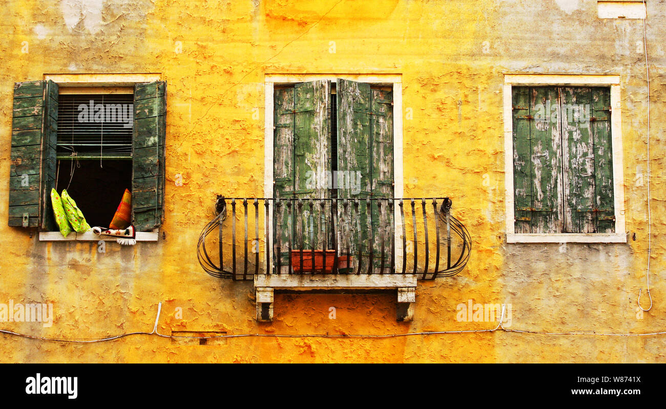 Traditional, typical window scene in the beautiful city of Venice, Italy. Sunshine yellow paint, shabby green window shutters. Such a romantic city. Stock Photo