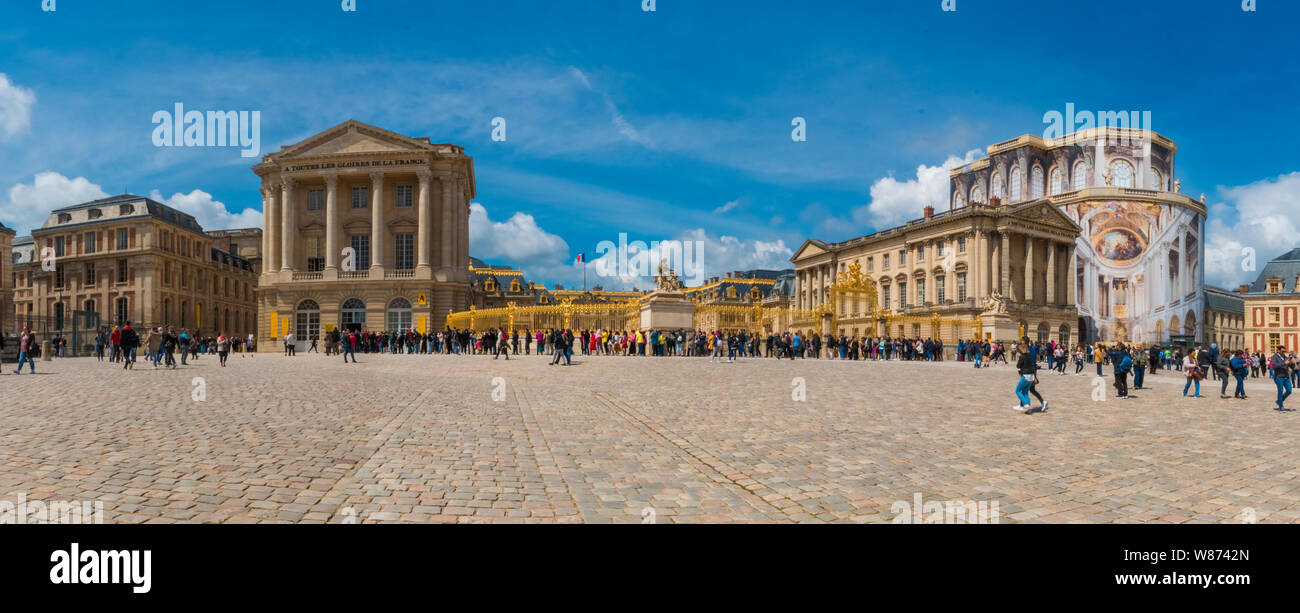 Lovely panorama picture of the Palace of Versailles in front of the golden royal gate at the entrance in the cobblestoned court of honour... Stock Photo