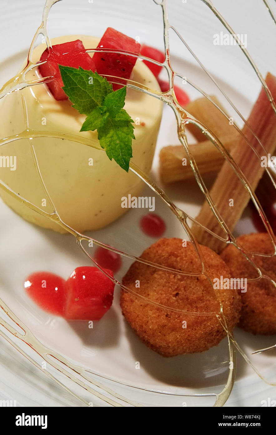 Panacotto with strawberry jellies and custard bon bons, candied sugar, churros and basil Stock Photo