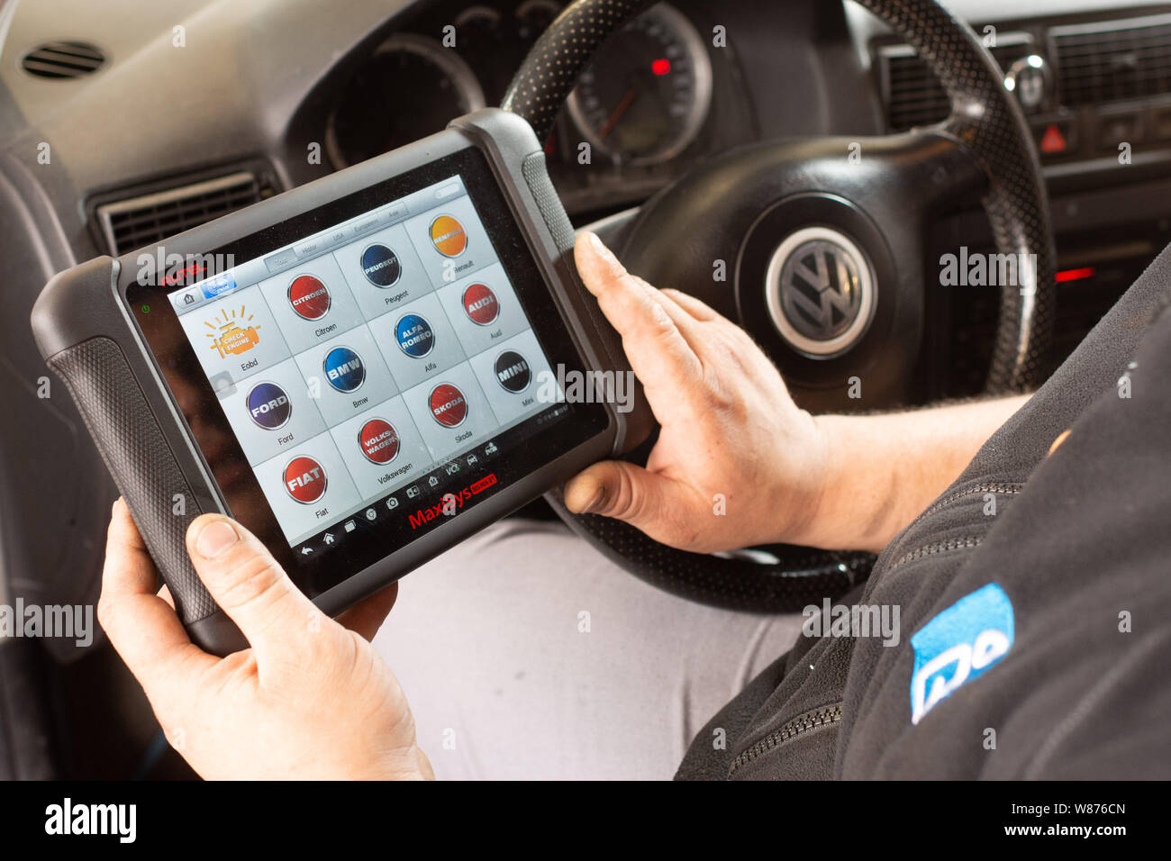 Garage: car mechanics. Worker using the touchscreen tablet of a car diagnostic tool in the front seat of a Volkswagen car, to detect any potential eng Stock Photo