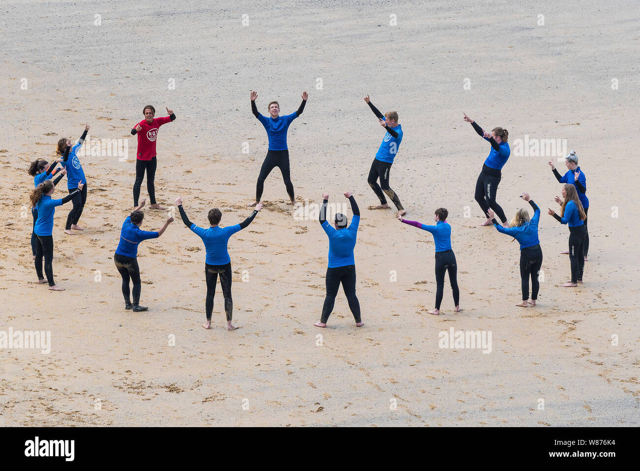 Novice surfers warming up before a surfing lesson on Great Gt. Western Beach in Newquay in Cornwall. Stock Photo