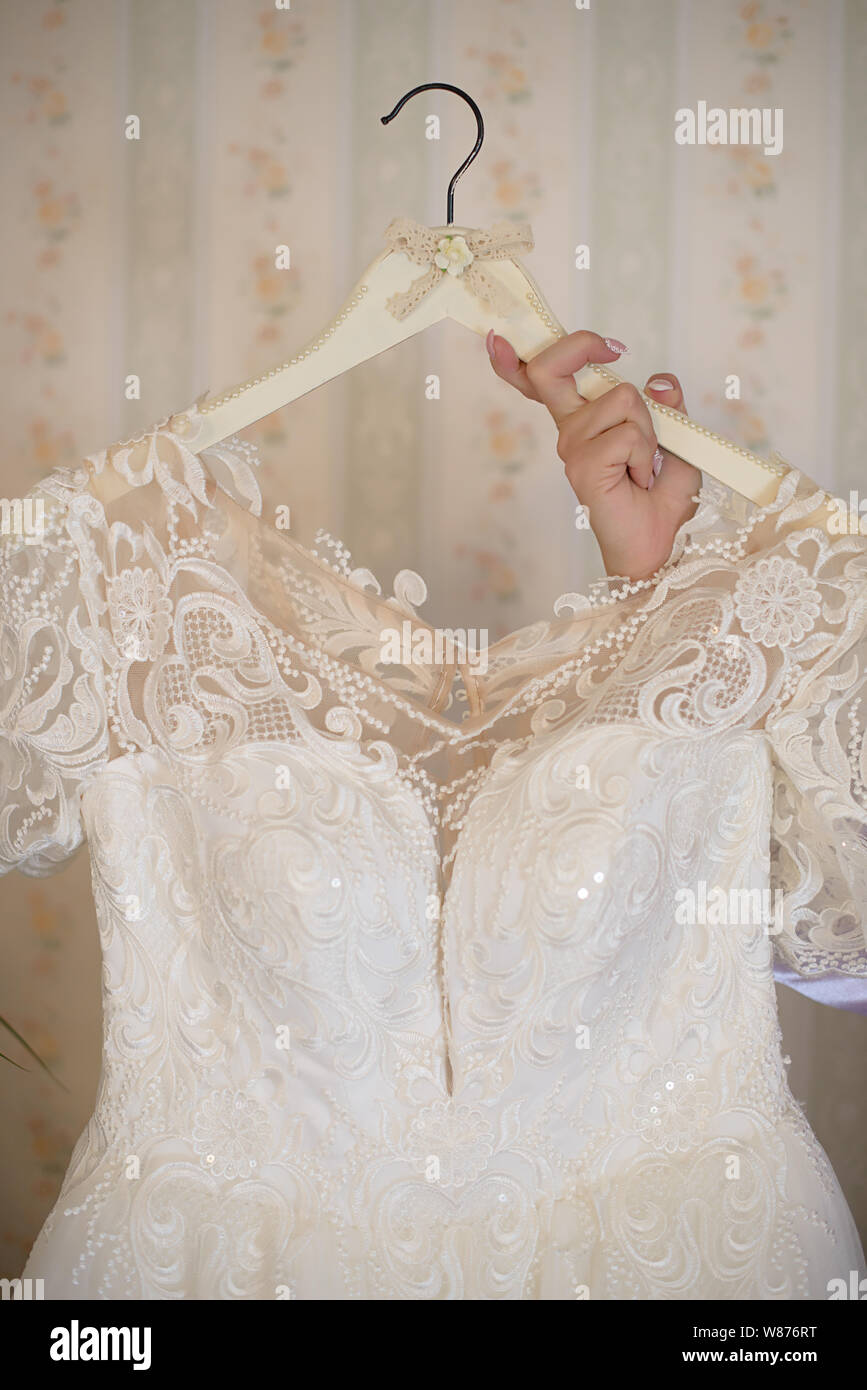 Woman hand holding an embroidered ivory white dress on a hanger featuring a sweetheart top, an elegant beige tulle lining and white sequins Stock Photo