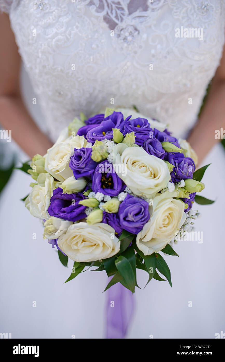 Caucasian female in beautiful lacy white dress holding a large round bouquet featuring ivory and purple roses at a wedding ceremony Stock Photo