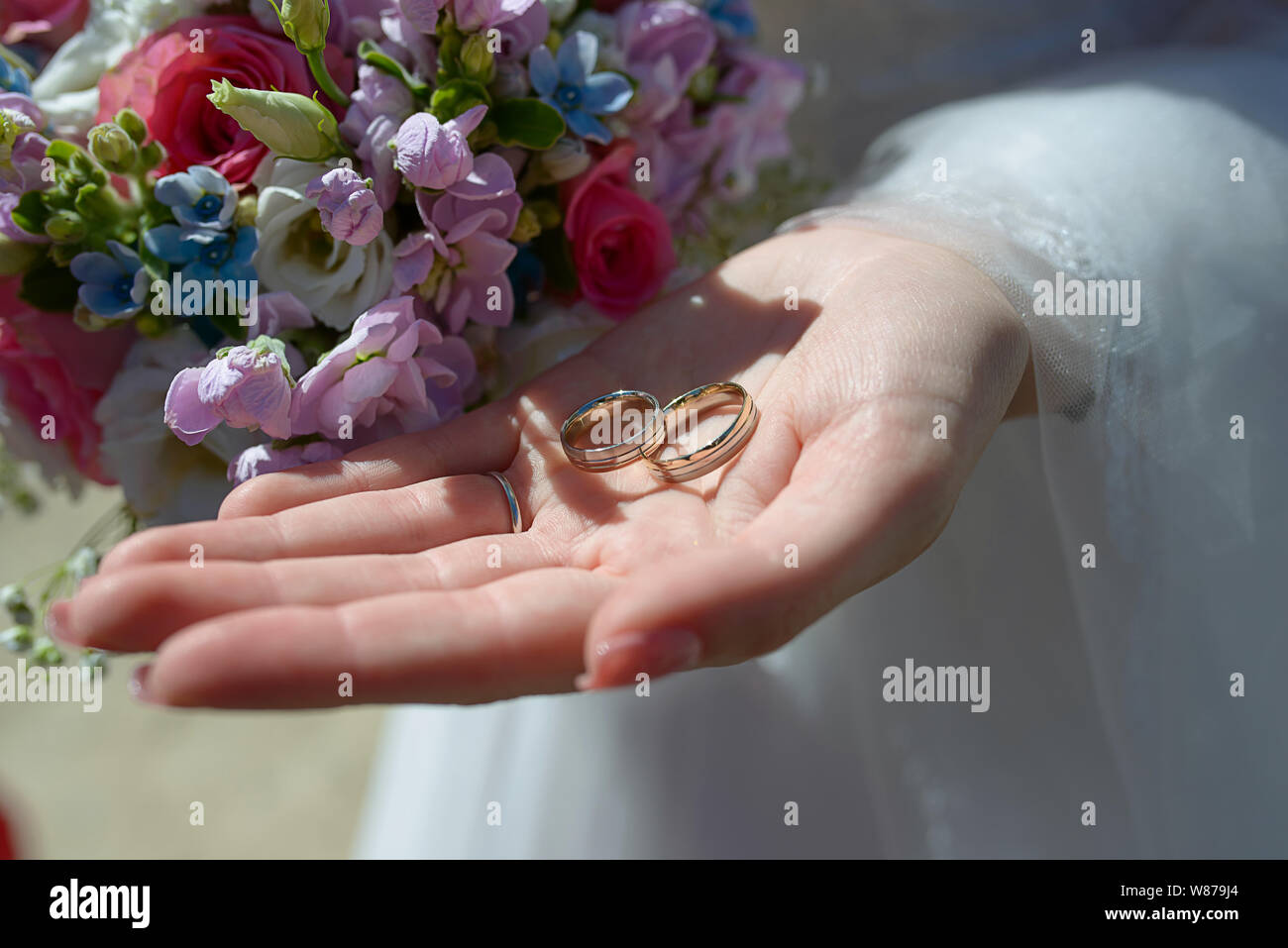 Bride at the wedding ceremony with focus on hands, in one hand holding a summer mixed flowers bouquet and in the other the wedding rings Stock Photo