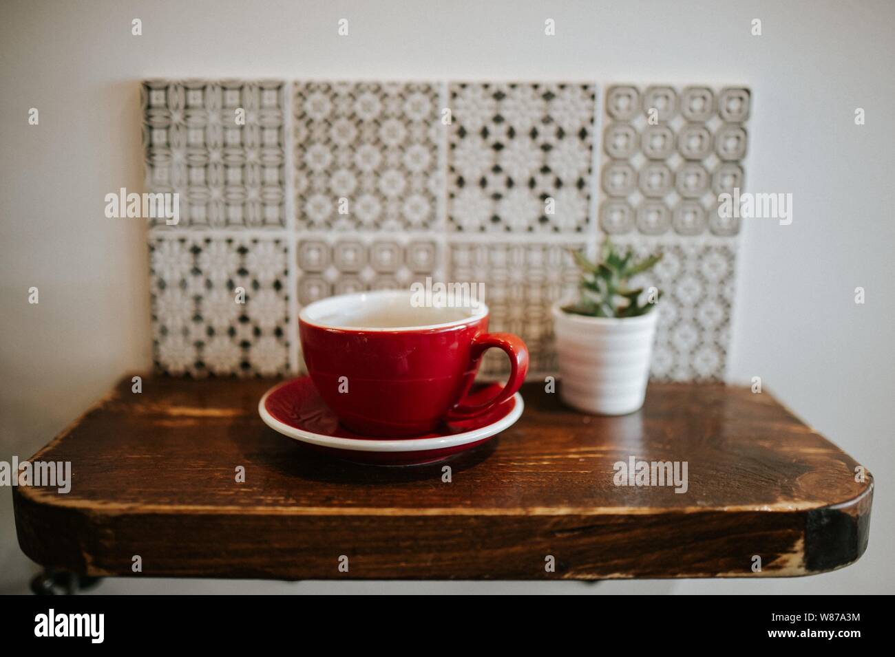 Closeup shot of a red ceramic cup and a flower pot on a small wooden surface Stock Photo