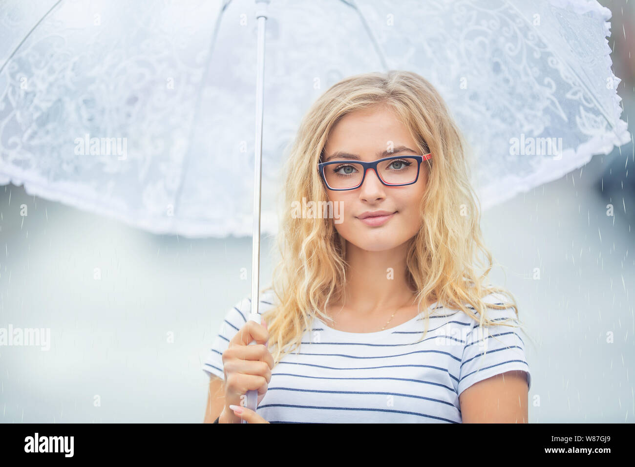Beautiful young blonde girl holding umbrella in summer rain. Stock Photo