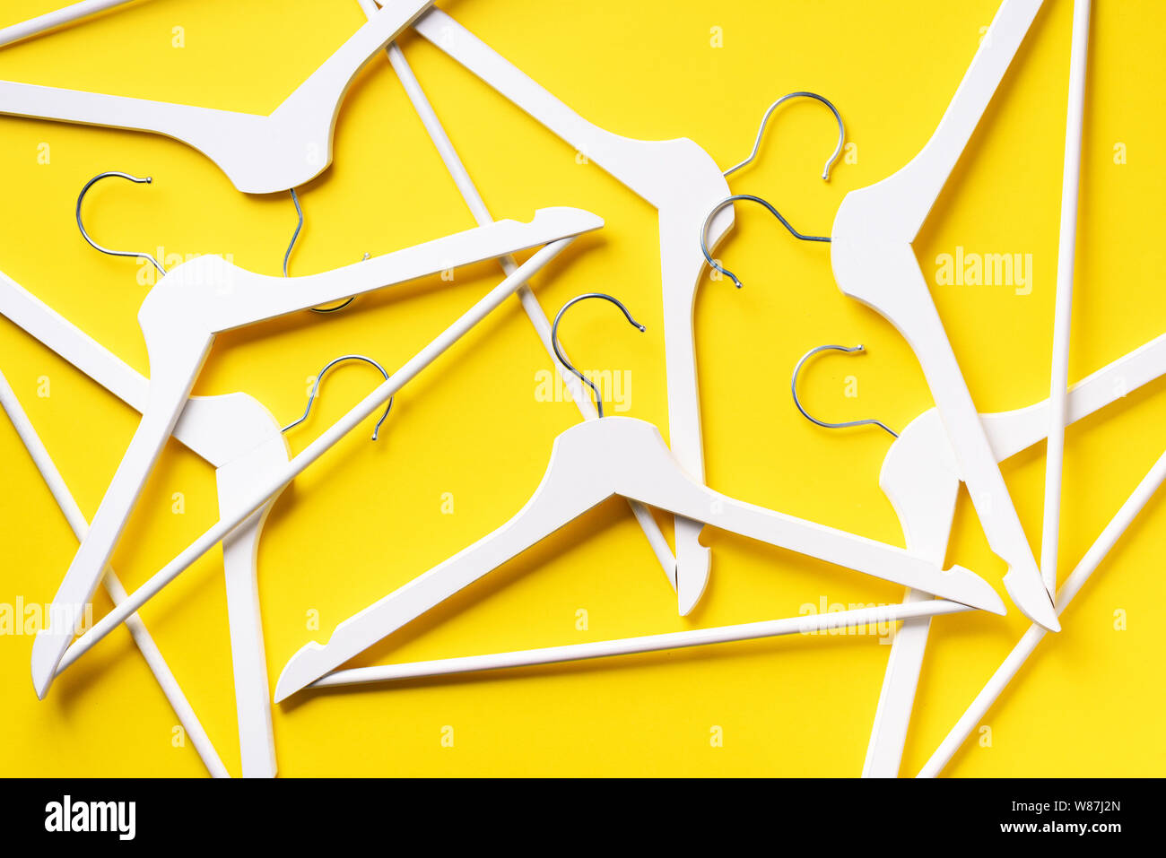 White clothes hangers on yellow background with copy space. Flat lay. Top view. Minimalism style. Creative layout. Fashion, store sale, shopping conce Stock Photo