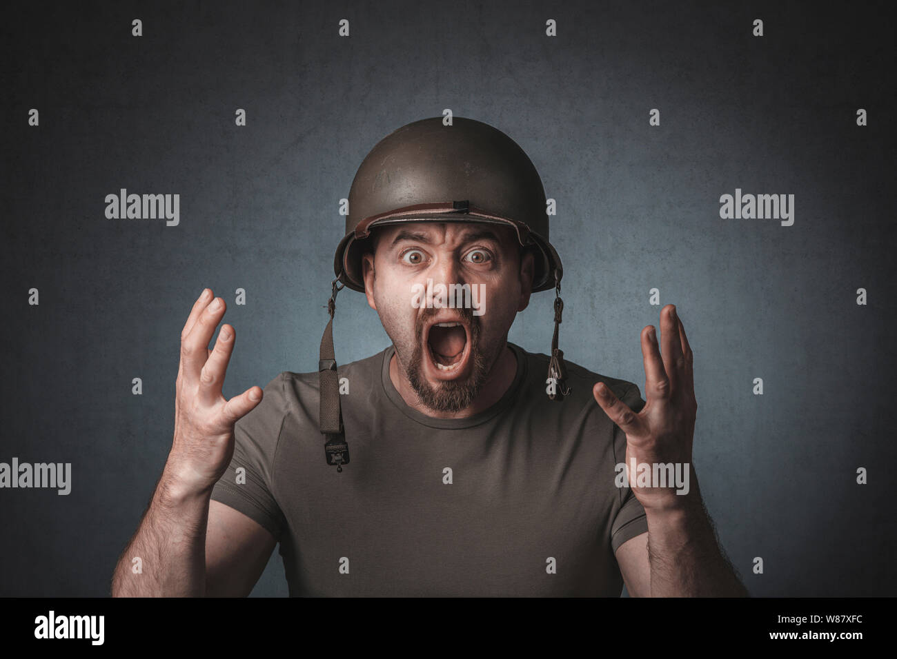 portrait of a screaming soldier with open arms. He is wearing a metal helmet. Stock Photo