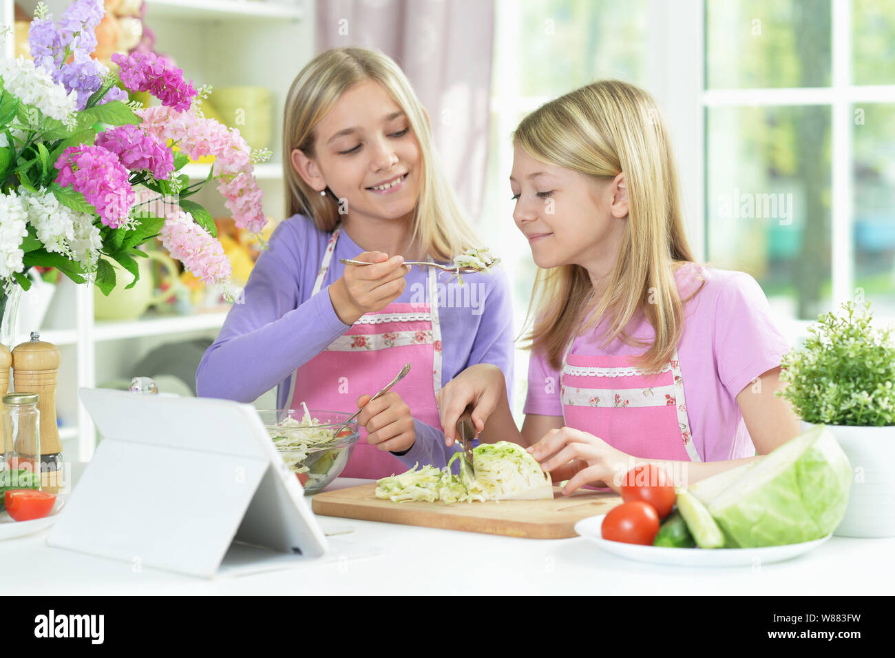 Two girls in pink aprons preparing salad Stock Photo