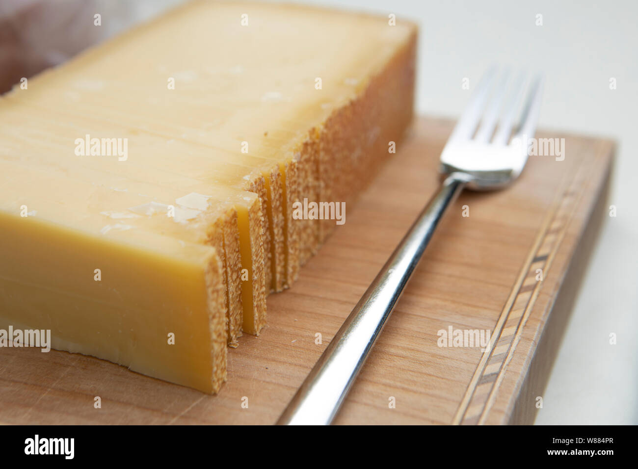 big slice of traditional Austrian hard cheese with rind on a wooden plate with a fork Stock Photo
