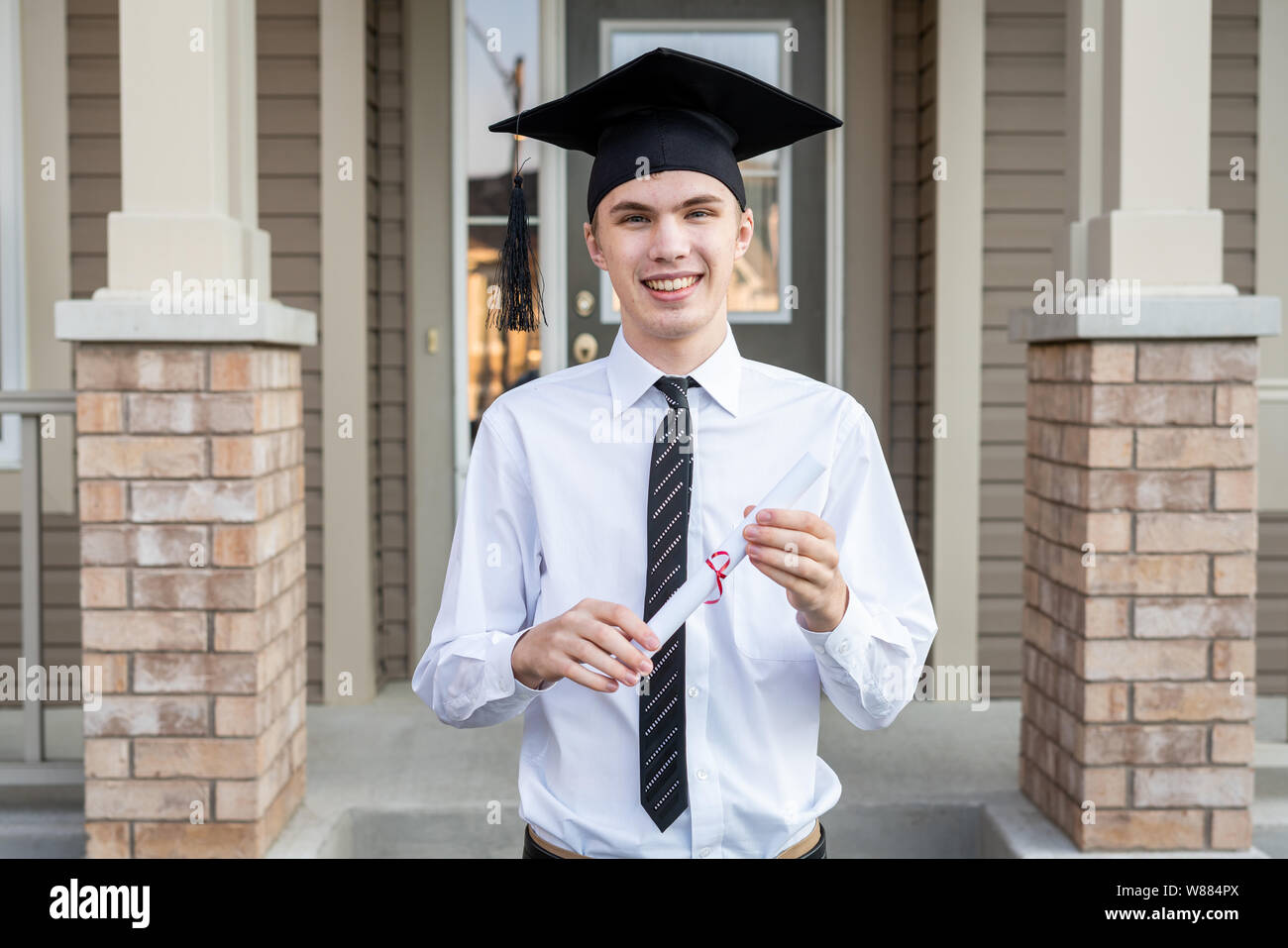 Young male student holding a diploma while wearing a graduation cap in ...