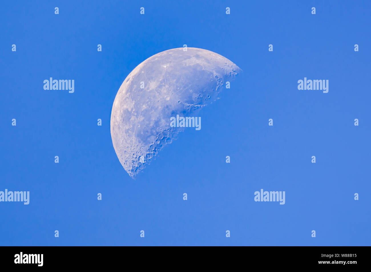 Third Quarter moon (AKA last quarter or half moon) phase of the moon in daytime against blue sky, in September. Stock Photo