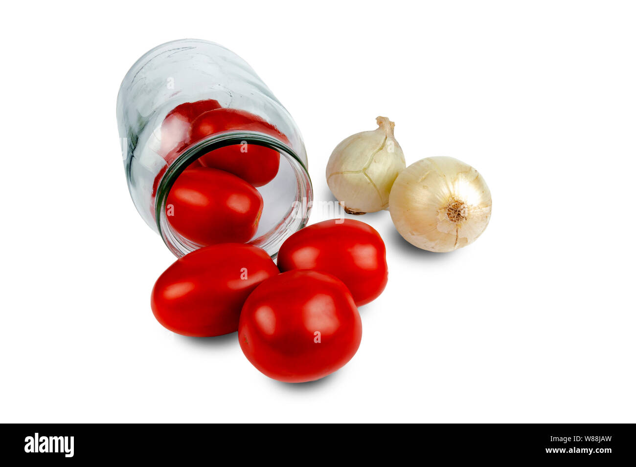 Tomatoes lie in a glass jar. Next to the jar are onions and garlic