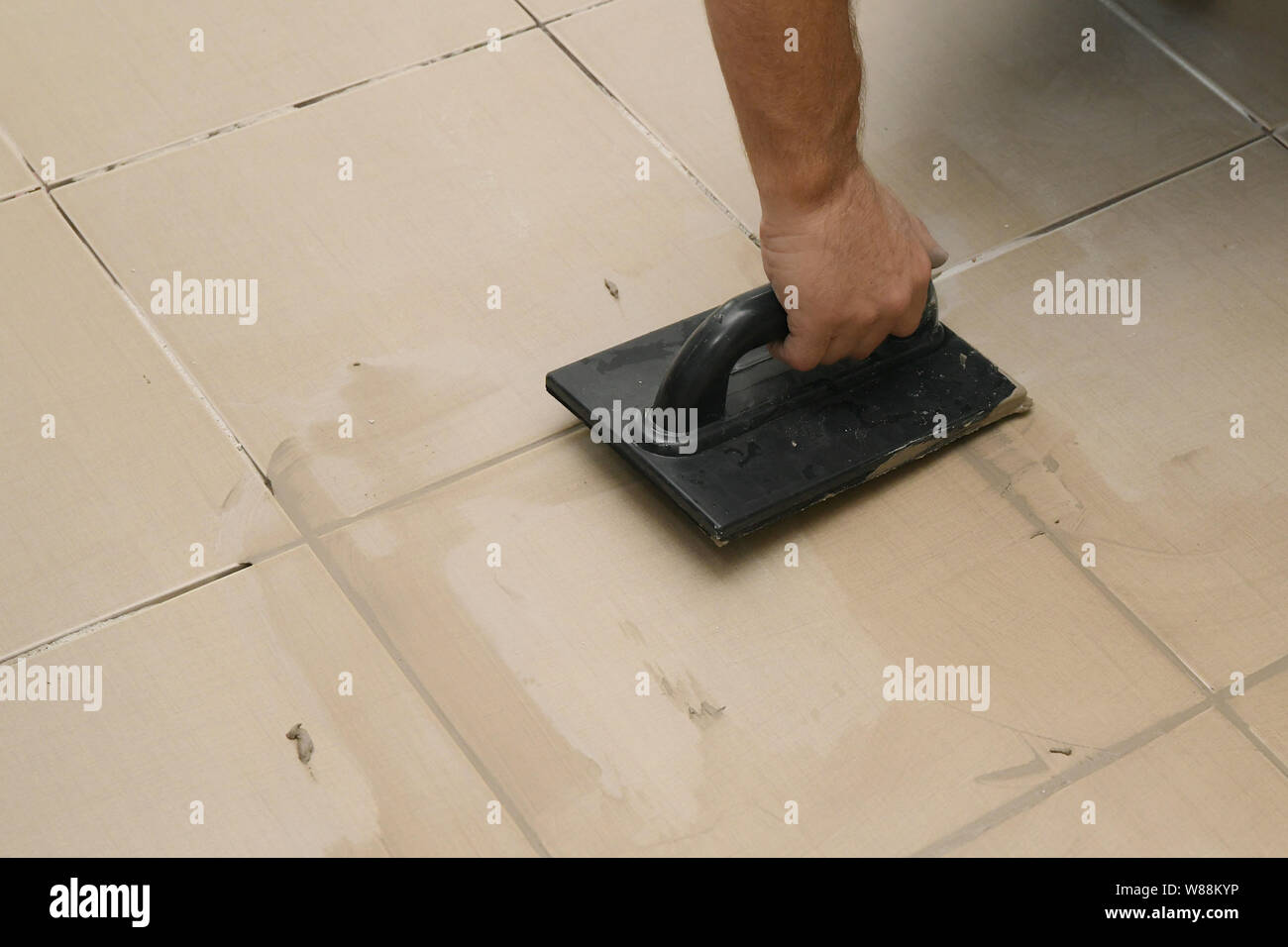 Worker putting fugue on tiles on the floor in corridor. Grouting ...