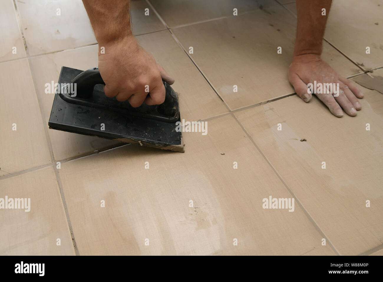 Worker putting fugue on tiles on the floor in corridor. Grouting ...