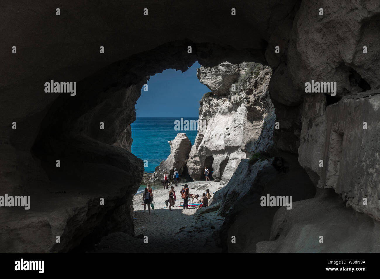 A beautiful beach accesible by a tunnel in a rock with some people. Sicily, Italy. Stock Photo