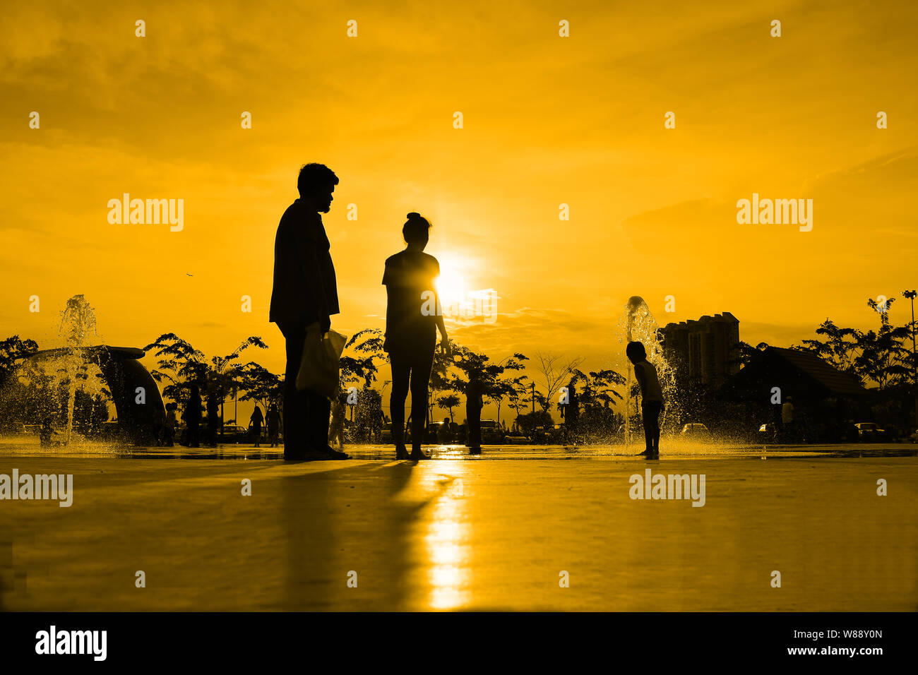 silhouettes of family playing in water fountain at sunset Stock Photo ...