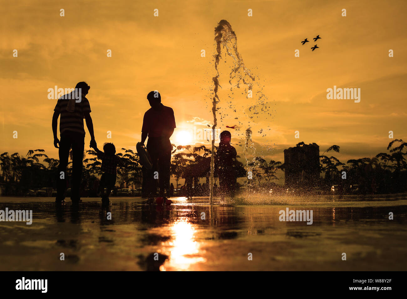 Silhouettes of family playing in water fountain at sunset Stock Photo ...