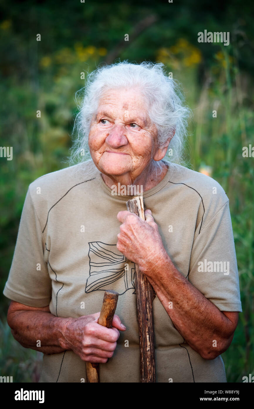 A closeup portrait of an old woman with gray hair smiling and looking up, resting her chin on a stick as if walking with a cane, face in deep wrinkles Stock Photo