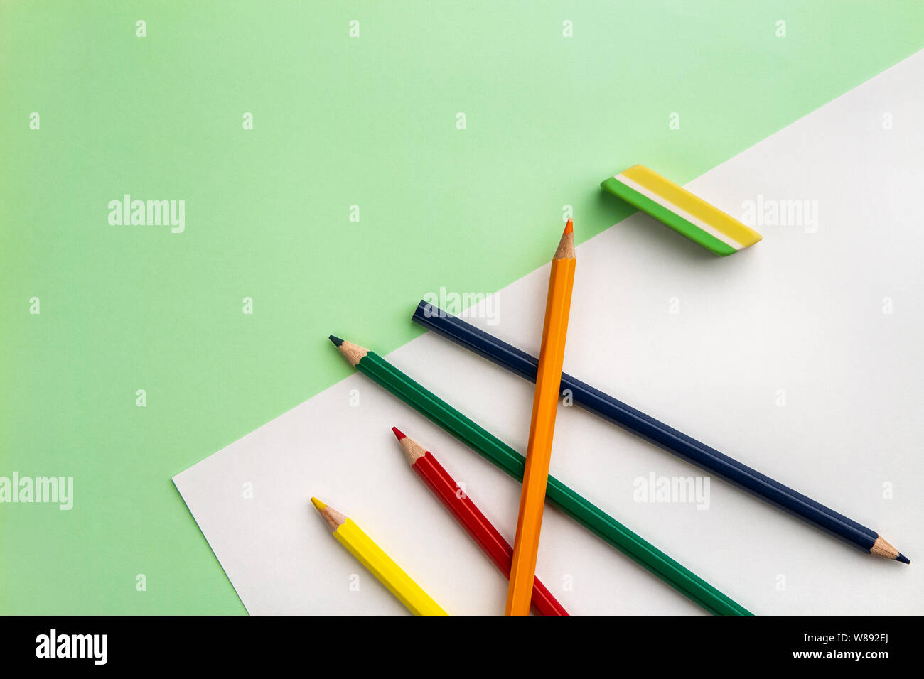 white sheet of paper, five pencils and an eraser on a light green paper background. Copyspace Stock Photo