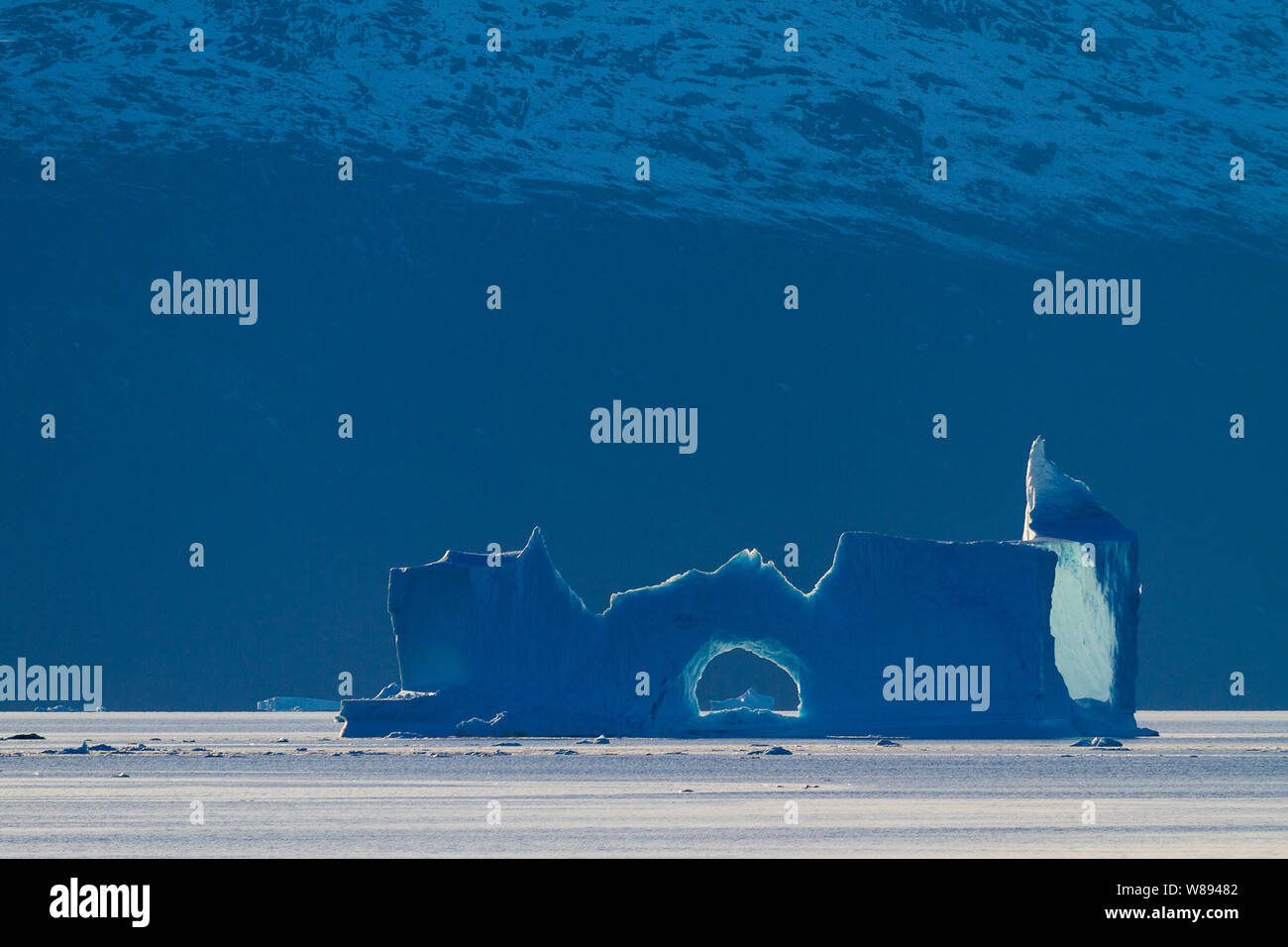 An absurd ice sculpture catches the fading light and is outlined against the darkening rock face in Ø fjord, Greenland Stock Photo