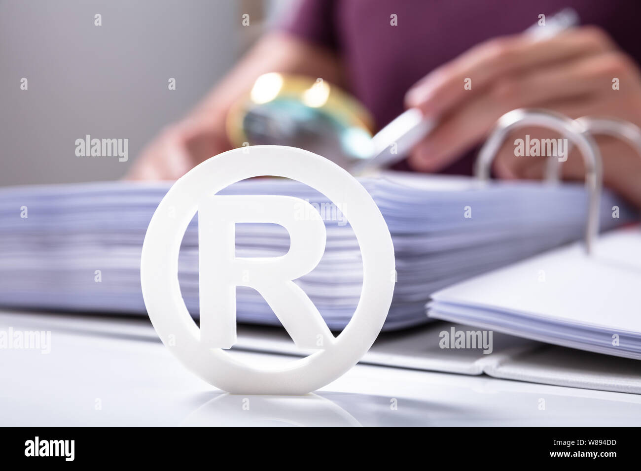Close-up Of White Registered Trademark Sign Near Documents Over Desk Stock Photo