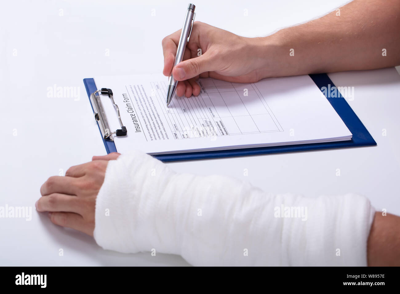 Close-up Of A Person's Hand Filling Health Insurance Claim Form Over White Desk Stock Photo