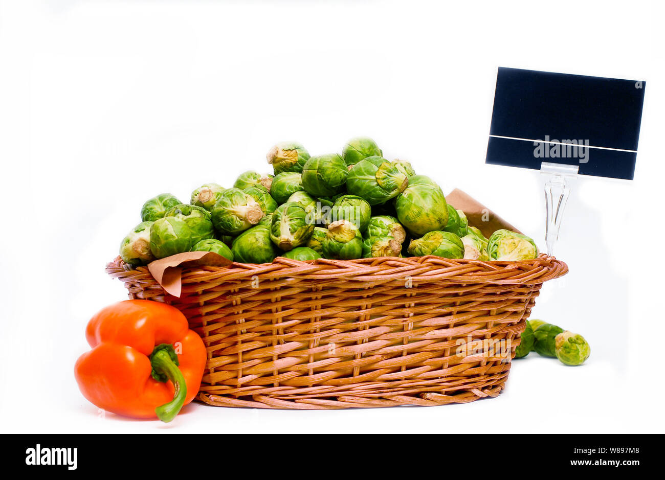 Wooden basket full of brussels sprouts and a orange capsicum on the side, for market use, isolated on whte with price tag. Stock Photo