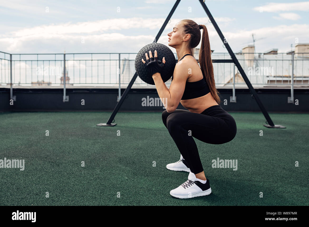 Side view of muscular woman holding a medicine ball while doing squats ...