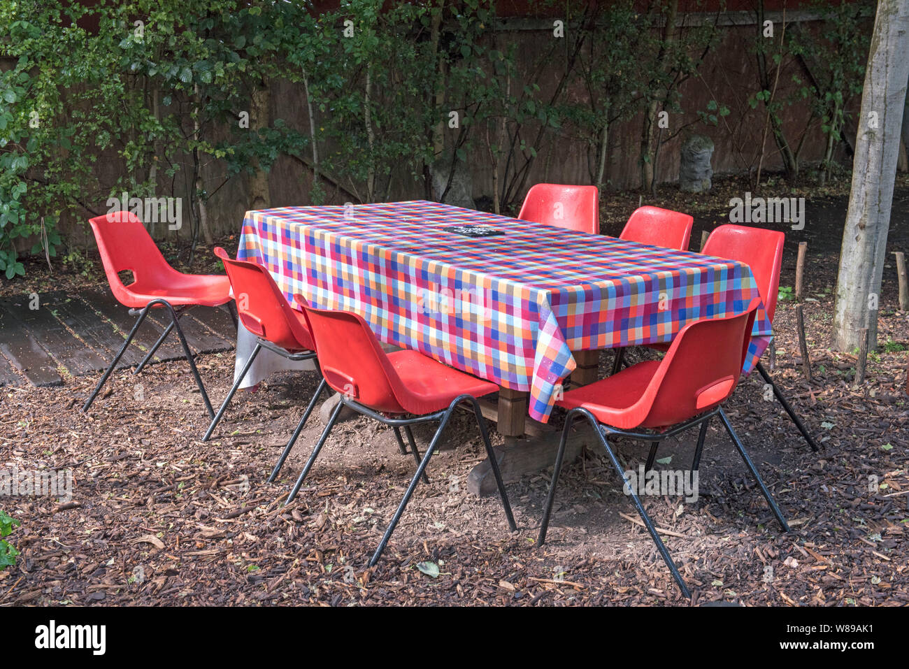 Empty table with chequred tablecloth and six red chairs outdoors, Dalston Eastern Curve Garden, London Borough of Hackney. Stock Photo