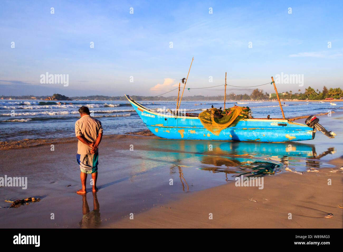 Mirissa, Sri Lanka - Decmber 30th 2016: Man stood by a traditional fishing boat ashore. The boats return early morning after a nights fishing. Stock Photo