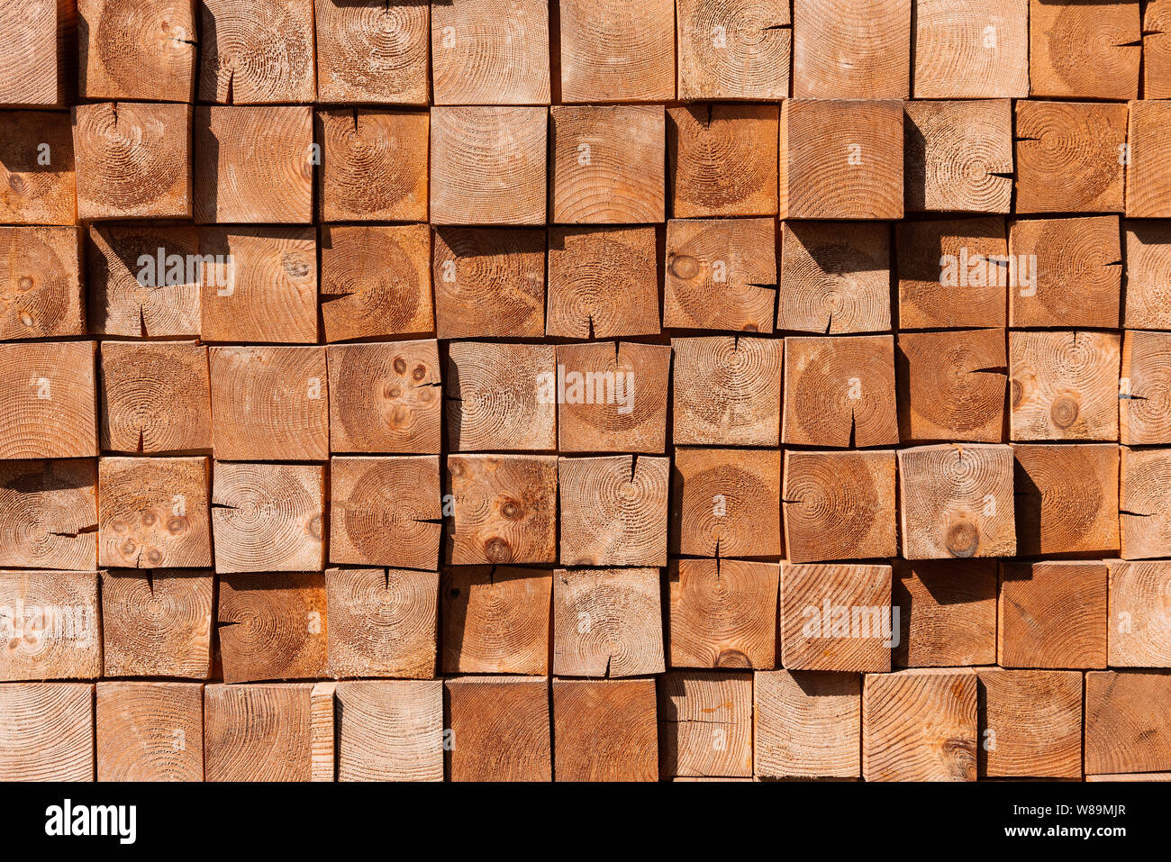 Square wooden blocks background. A wall made of many trees. Cozy interior in Scandinavian style. Natural brown backdrop. Deforestation concept. Stock Photo
