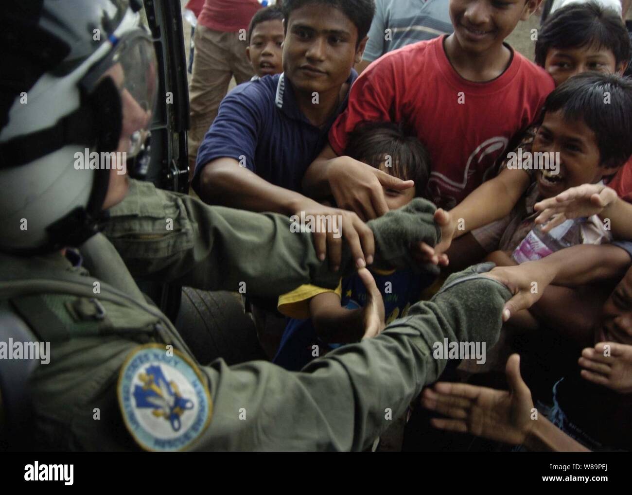 A U.S. Navy aircrewman assigned to Helicopter Anti-Submarine Squadron 2 shakes the hands of local citizens after delivering food and water to their village in Indonesia on Jan. 6, 2005.  The aircraft carrier USS Abraham Lincoln (CVN 72) and its embarked Carrier Air Wing Two 2 are operating in the Indian Ocean off the coasts of Indonesia and Thailand in support of Operation Unified Assistance. Stock Photo