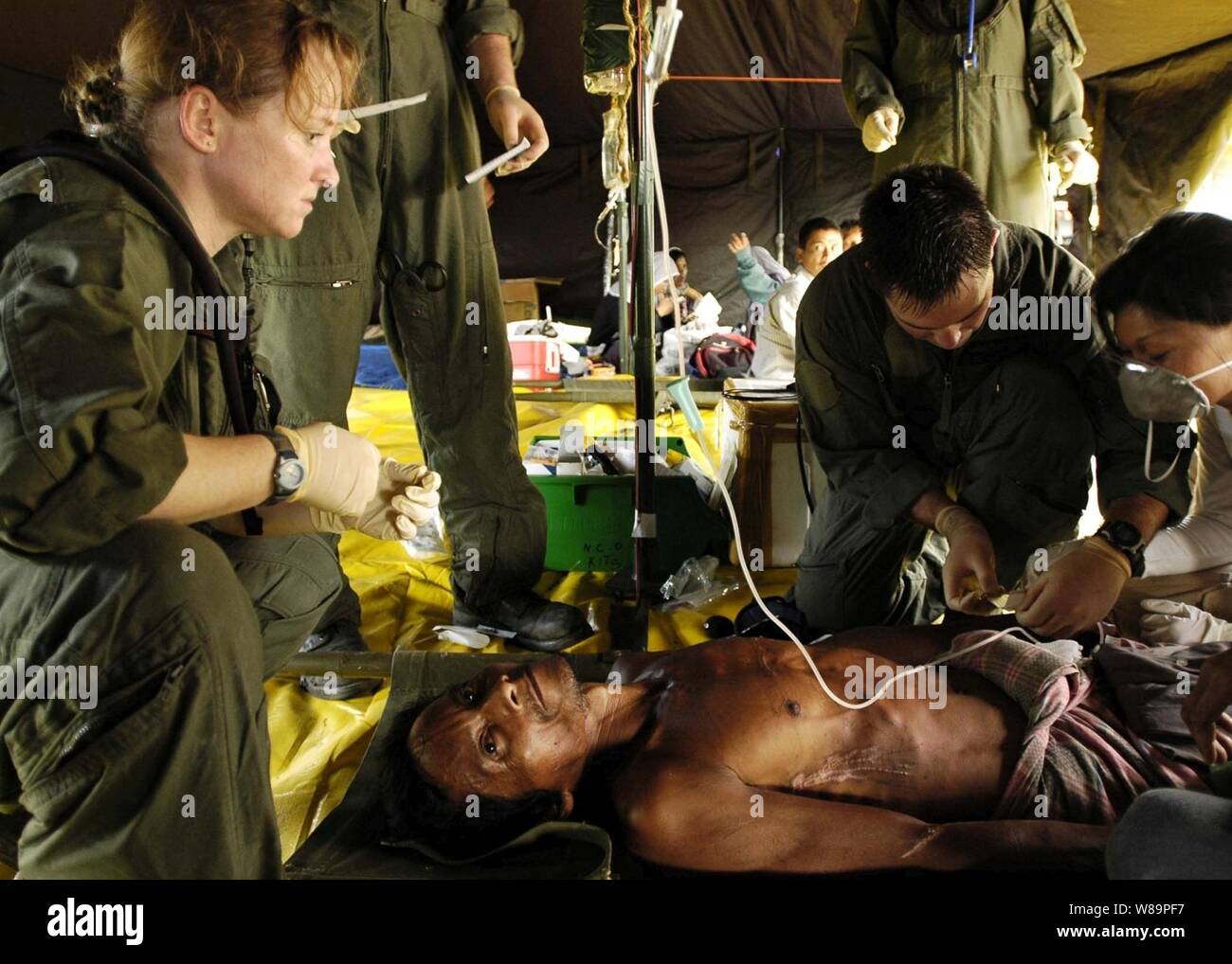 Navy Petty Officer 1st class Rebecca McClung (left) and Chief Petty Officer Jim Jones (right) tend to an injured Indonesian man who was medically evacuated from a coastal village on the island of Sumatra, Indonesia, on Jan. 3, 2005.  Medical teams from the aircraft carrier USS Abraham Lincoln (CVN 72) and the International Organization for Migration have set-up a triage site on Sultan Iskandar Muda Air Force Base, in Banda Aceh, Sumatra.  The two teams are working together with members of the Australian Air Force to provide initial medical care to victims of tsunami-stricken coastal regions. T Stock Photo
